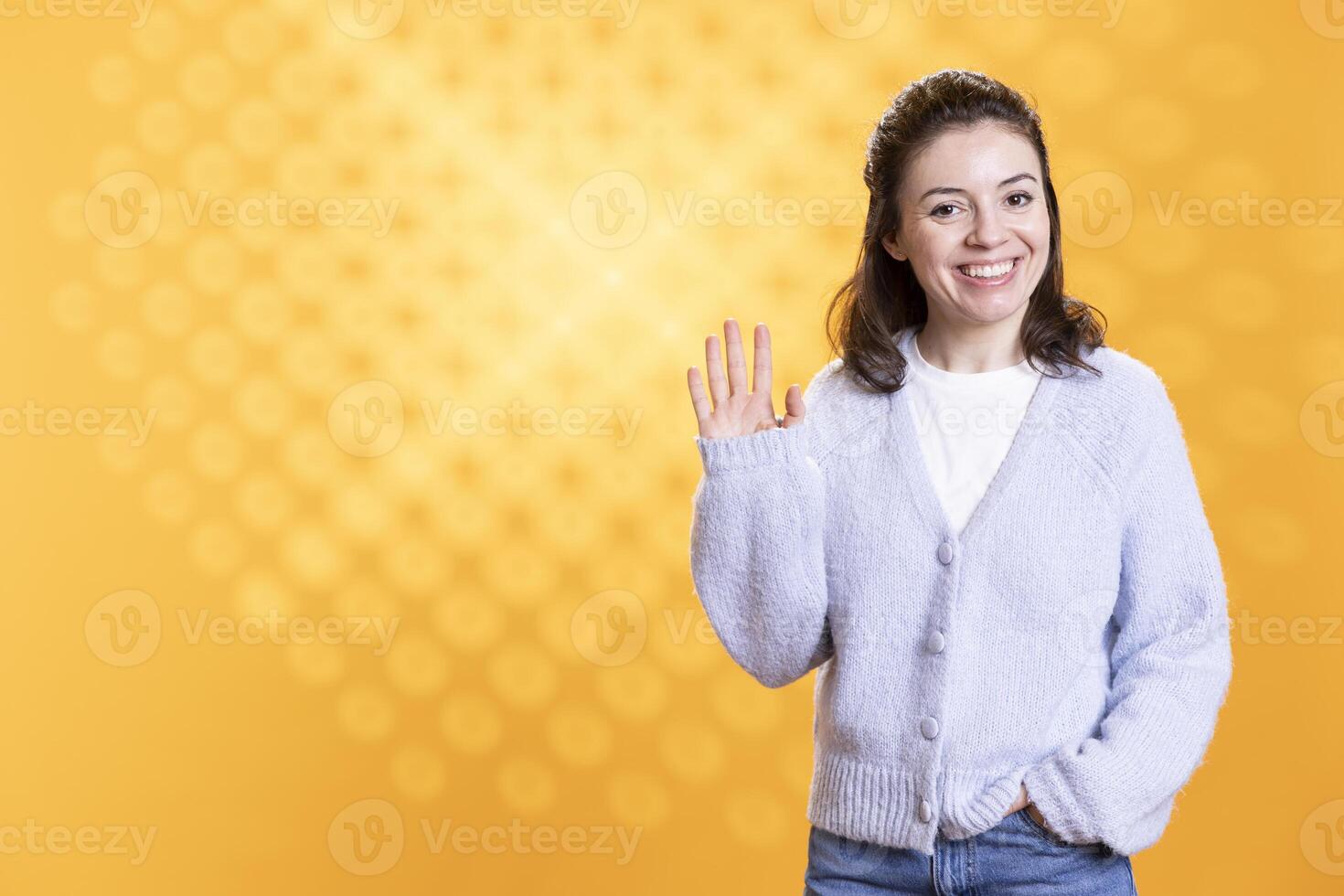 Cheerful woman happily doing salutation hand gesture, feeling optimistic. Portrait of joyous caucasian person raising arm to greet someone, gesturing, isolated over yellow studio background photo