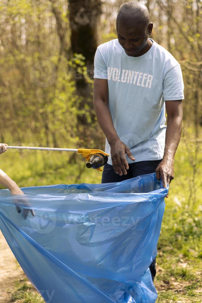 Volunteers picking up garbage and plastic bottles from the forest, protecting the natural habitat and doing voluntary work. Activists team cleaning the woods, recycling waste. photo