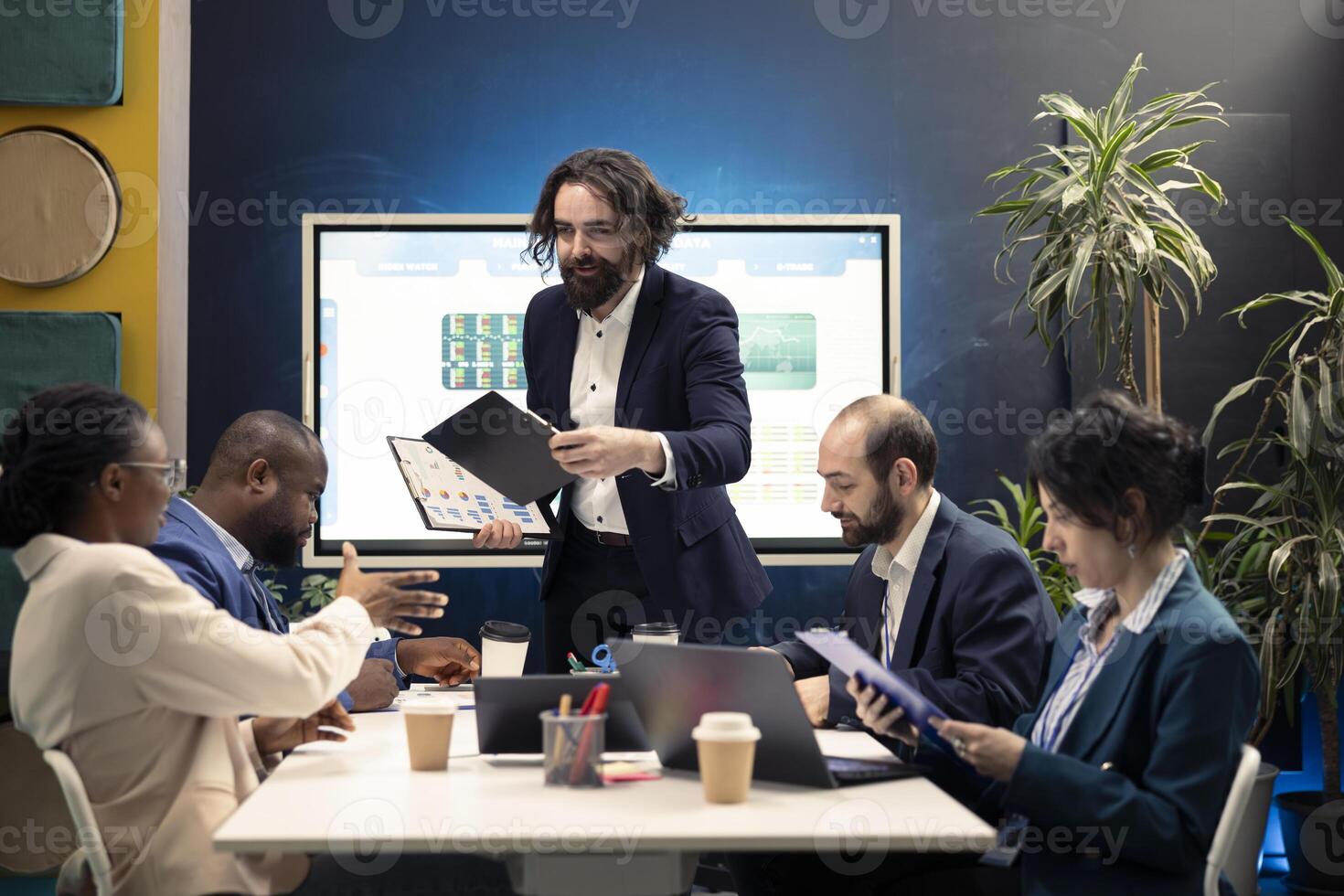 Executive team develops strategic plans and financial projections during meeting, manager provides clipboards with data reports. Employees allocating essential resources from capital funds. photo