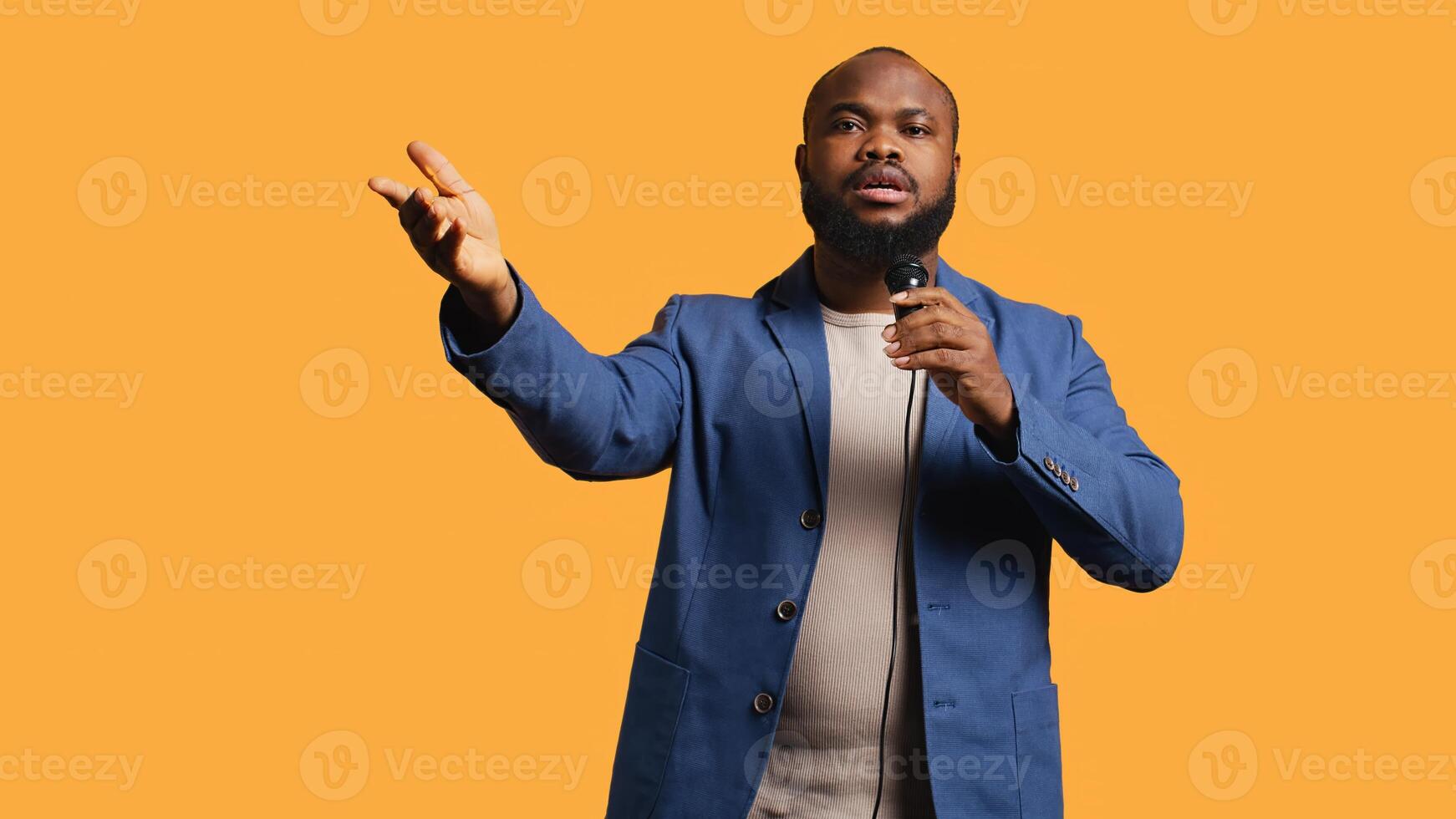 African american motivational speaker holding monologue using microphone, gesturing with hands, studio background. Energetic BIPOC speaker talking during presentation using mic, doing speech, camera B photo