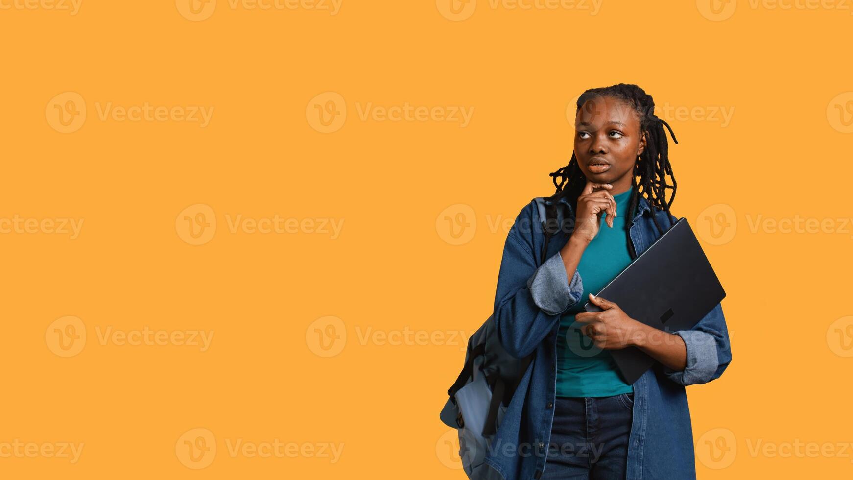 Pensive woman carrying laptop, doing thinking gesture, memorizing information for school exam, studio background. Student holding notebook, remembering before university assessment, camera B photo