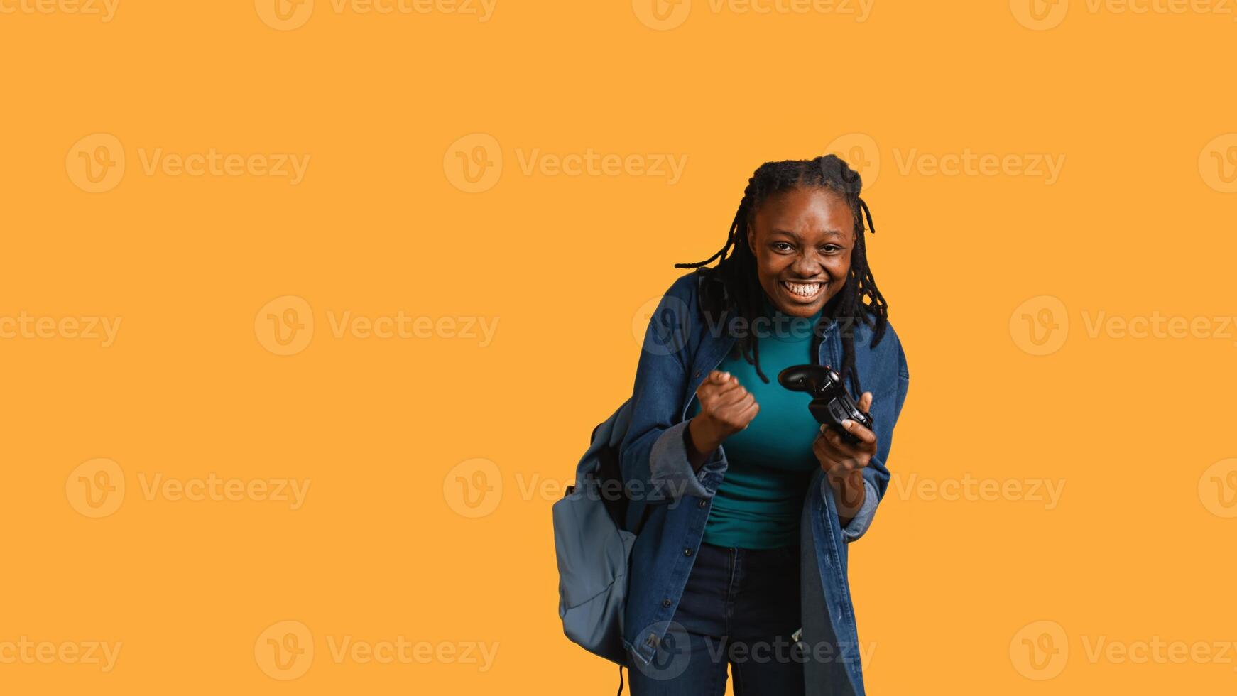 Euphoric african american woman playing intense gaming console game, celebrating win, studio background. Ecstatic young girl using controller, excited after being victorious in videogame, camera B photo