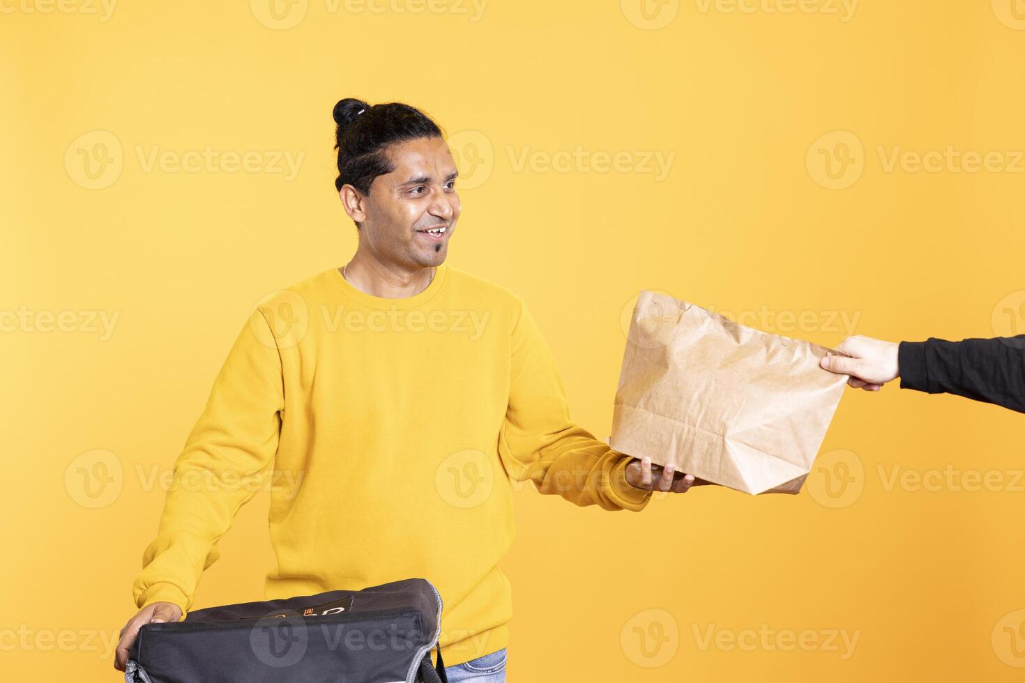 Delivery man arriving to client address with takeaway order in thermal backpack, handing it. Food courier removing packaged meal out of transportation bag, giving it to man, studio background photo