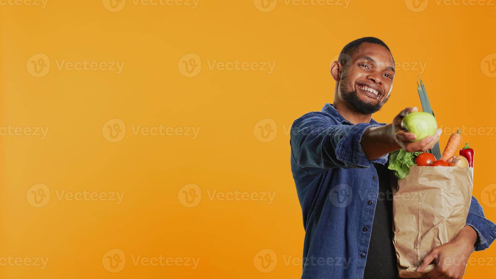 African american man presenting a freshly harvested green apple, showing the organic bio fruits in front of the camera. Happy person advocating for healthy eating and vegan nutrition. Camera B. photo