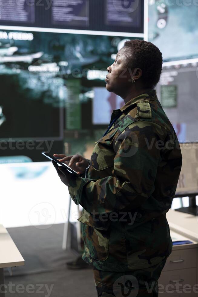 Woman trooper analyzing crucial battlefield data on a big screen in military control center, base of operations. Female engineer collecting and comparing information, reconnaissance. photo