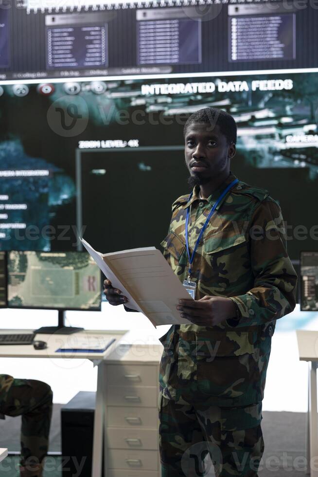 Navy operations specialist reading new mission case files in command center, working with satellite real time data projection on a big screen. Soldier enlisted in national army defense program. photo