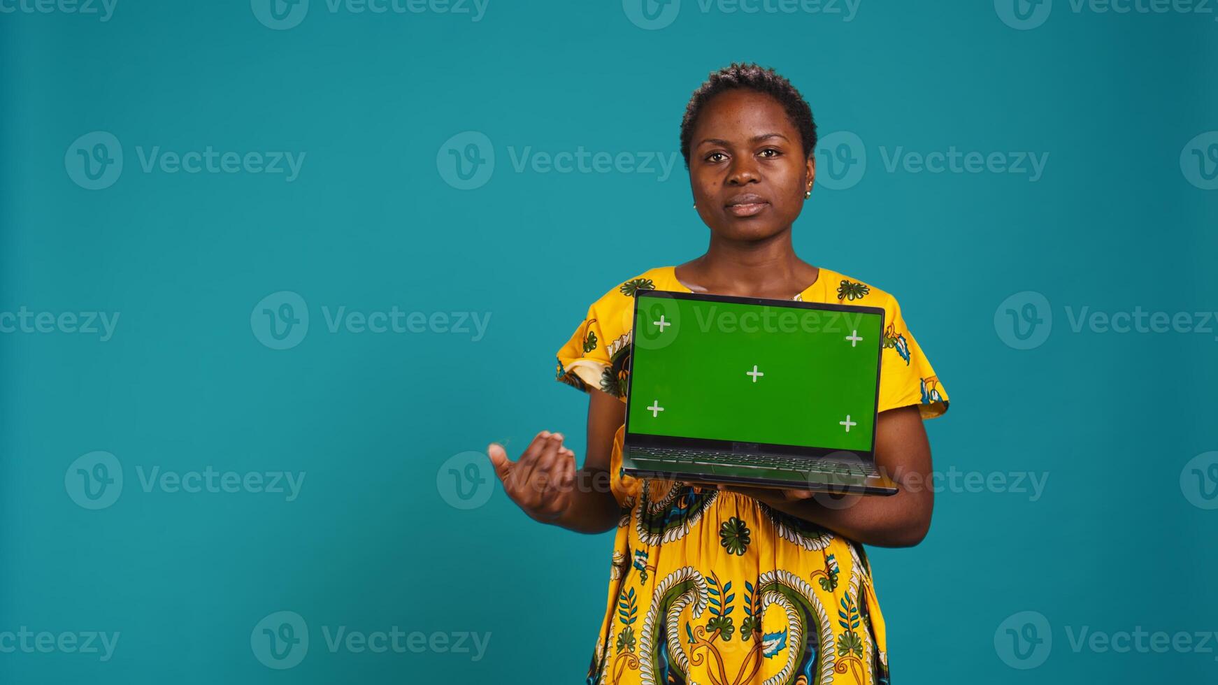 Confident happy person posing with a copy space mockup on laptop, create an advertisement with isolated display in studio. Young woman in ethnic attire with floral elements. Camera B. photo