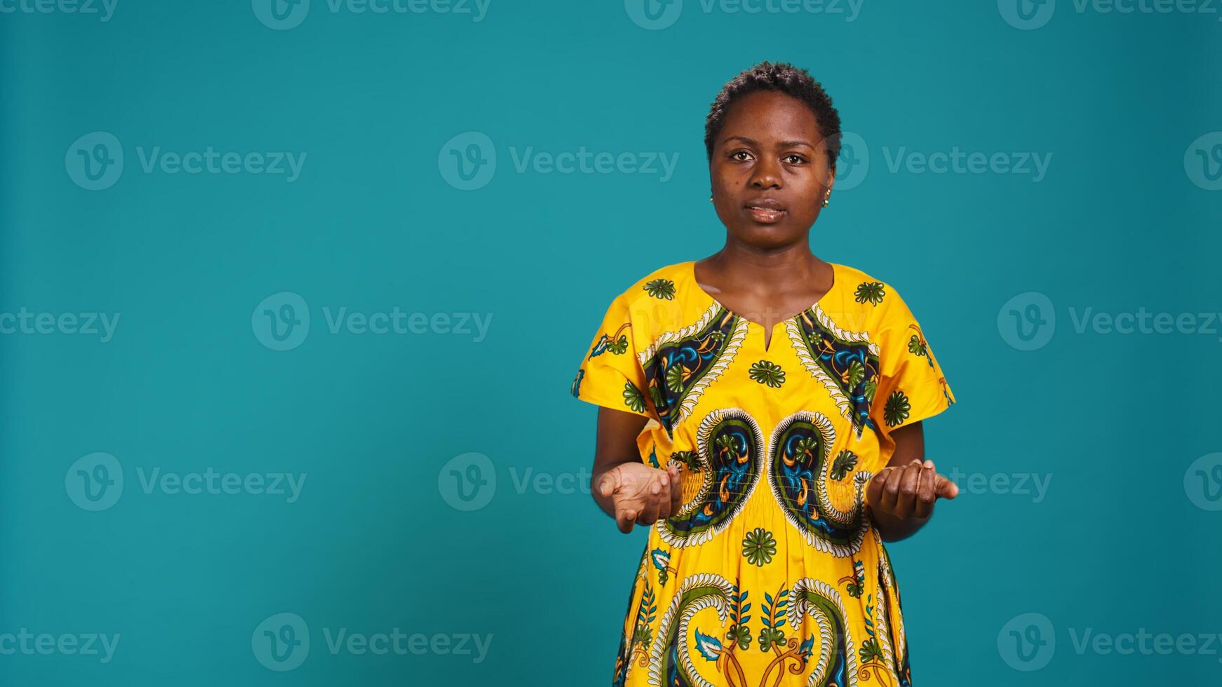 Young adult feeling uncertain and raising shoulders in studio, being unsure and indecisive against blue background. Doubtful clueless girl acting confused about something unknown. Camera B. photo