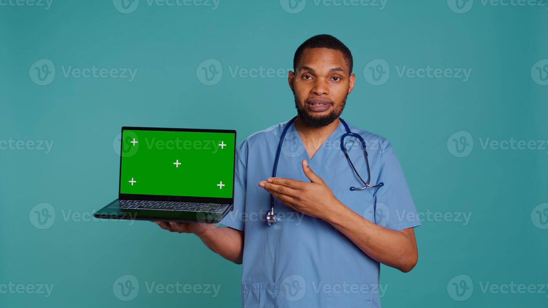 Portrait of african american doctor in medical scrubs using isolated screen laptop. Hospital staff member doing presentation using chroma key notebook, showing patient treatment plan, camera B photo