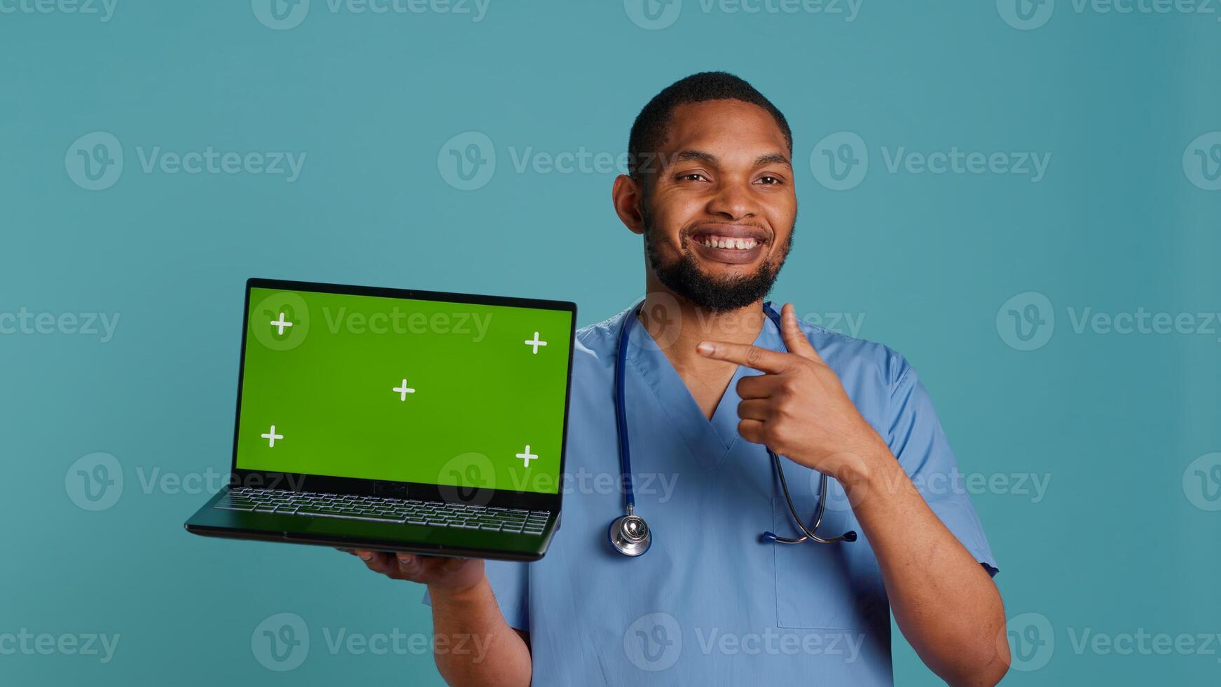 Portrait of practitioner showing medical instructions on green screen laptop. Healthcare employee holding chroma key notebook, isolated over studio background, camera A photo