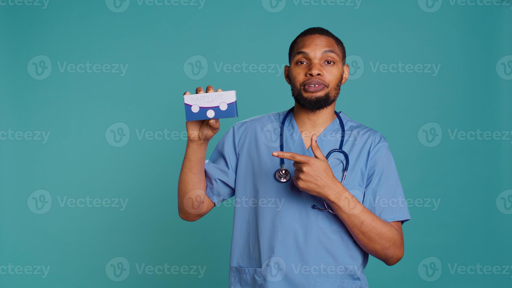 Portrait of medic in scrubs holding medicine package for patients suffering from illnesses, studio backdrop. Hospital staff member recommending tablets for patients with chronic diseases, camera B photo