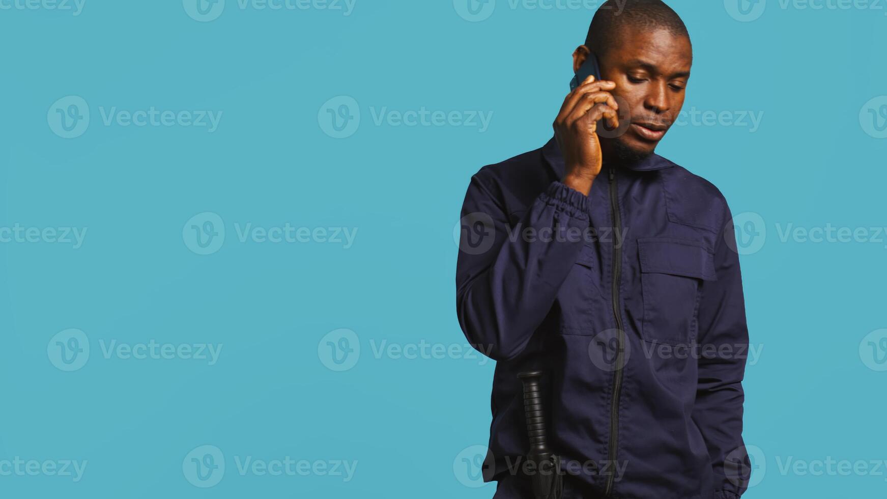 Security guard using cellphone to make call to friends during protection job shift. Portrait of bodyguard in telephone call with mates at work using phone, studio background, camera B photo