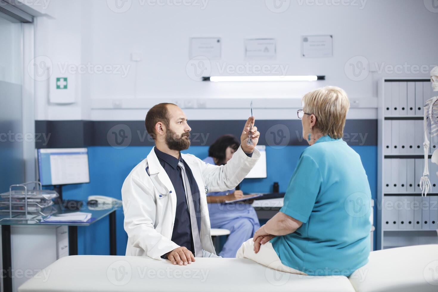 Mature patient sees specialist to recover from back discomfort. Physiotherapist offers advice on workouts and medical assistance. Digital X-ray imaging in a hospital consulting room. photo