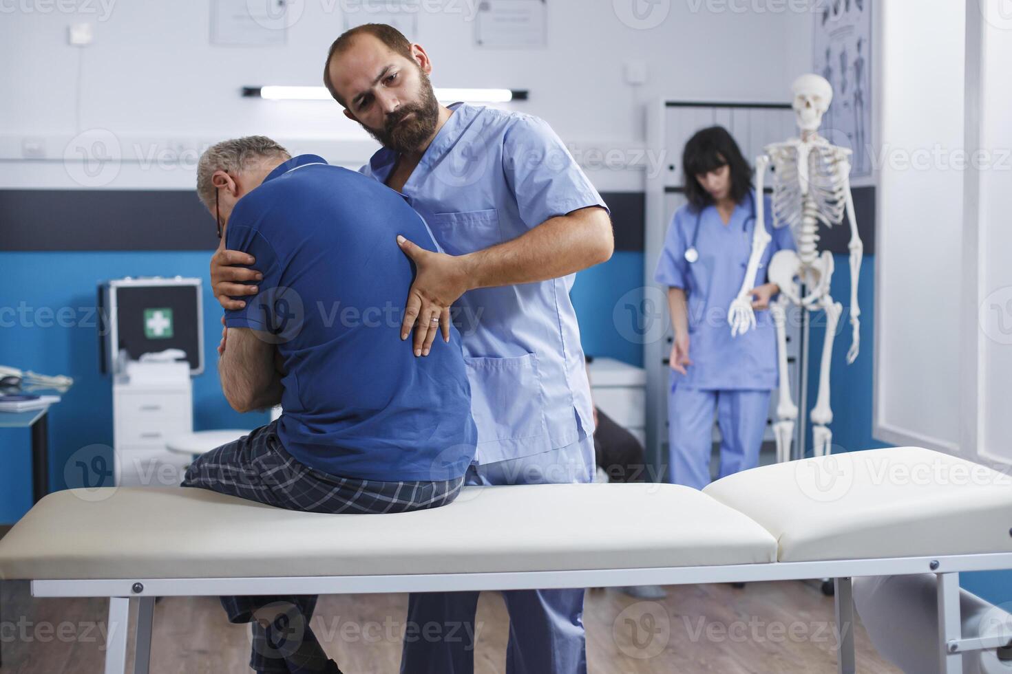 Osteopathic nurse gently extends spine of elderly patient with injury as part of physiotherapy. Chiropractor provides aid to gentleman experiencing back pains, aiding in physical recovery. photo