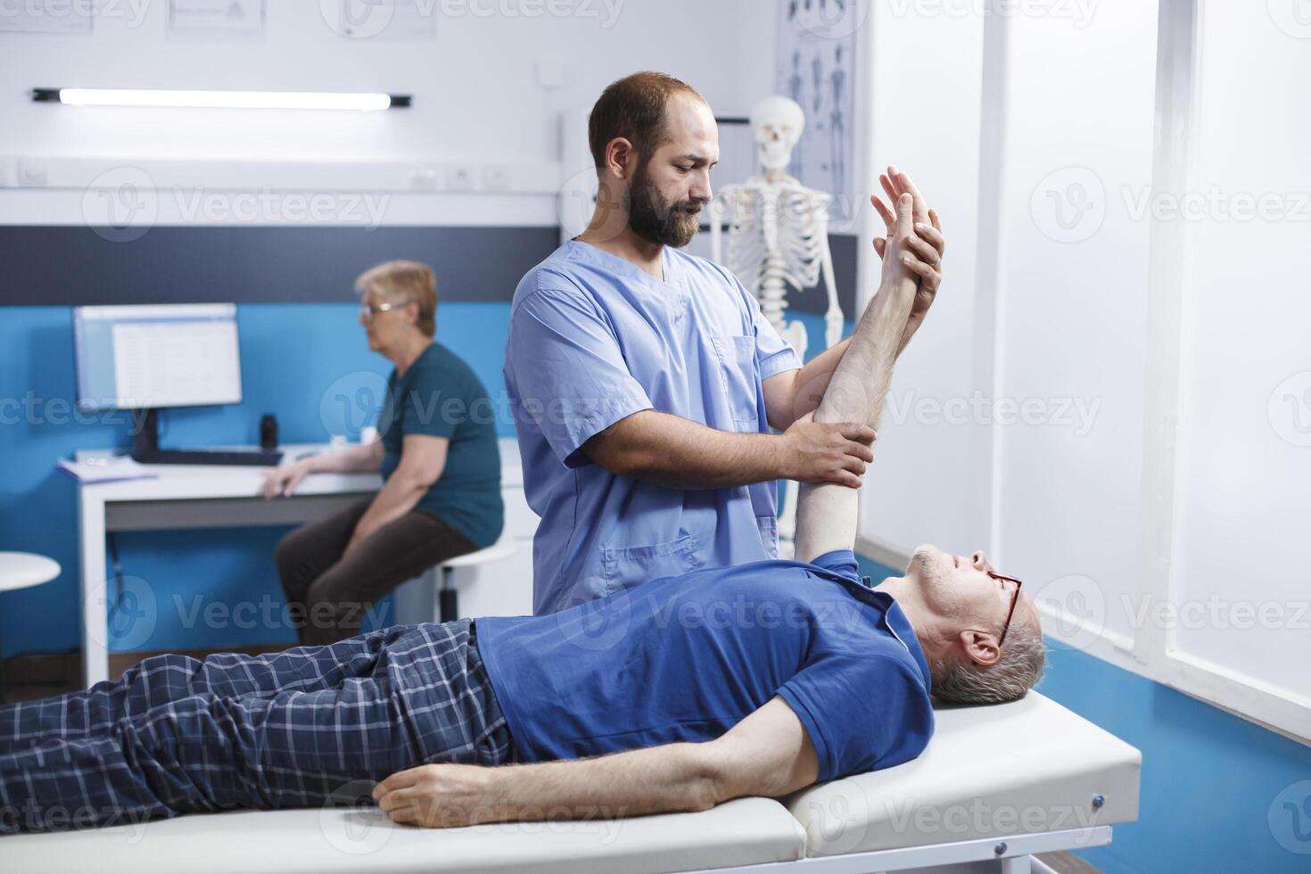 Chiropractor in blue scrubs uses osteopathic massage to help elderly male patient heal their hand muscles. Medical nurse helps old man extend his arm joint as part of his physical therapy. photo