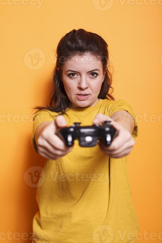 Portrait of focused woman in front of camera holding wireless controller. In studio, young female adult engaged in an online game, using joystick to play on console. photo