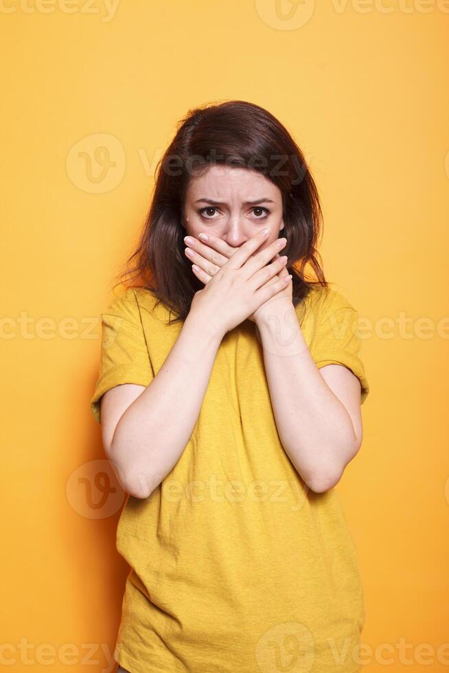 Portrait of brunette lady covering her mouth with both hands in response to shocking and unbelievable situation. Caucasian female person with worried and terrified expression on her face. photo
