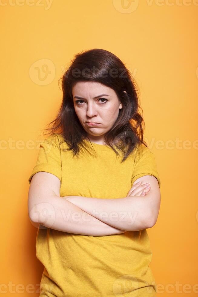 Woman standing in studio with crossed arms, disapproving and displeased facial expression on camera. Portrait of a dissatisfied person striking a grumpy and solemn expression. photo