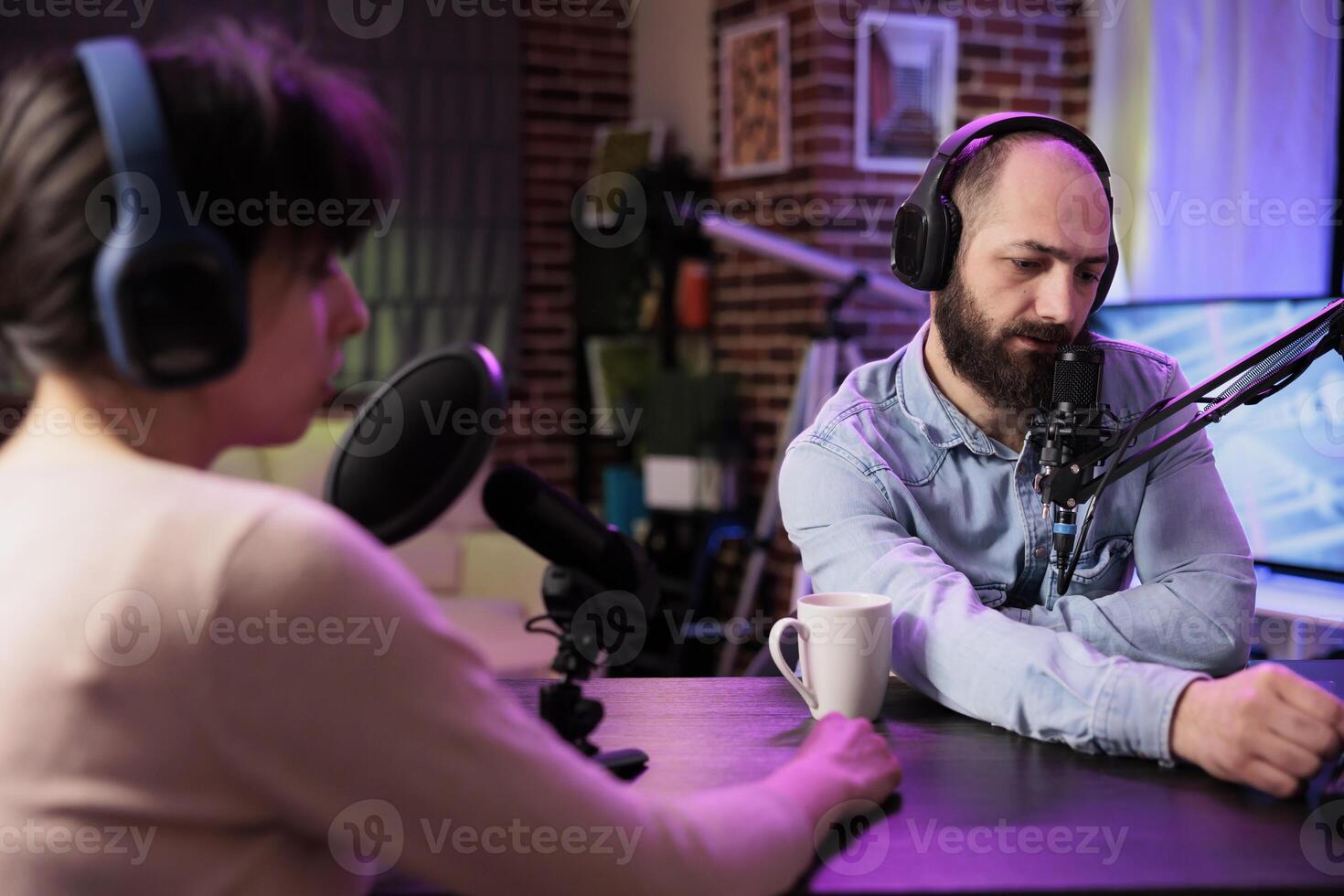 Cohosts streaming podcast using professional vlogging gadgets to live broadcast debate on politics vlog channel. Man and woman meeting in neon lights decorated living room studio to film show photo
