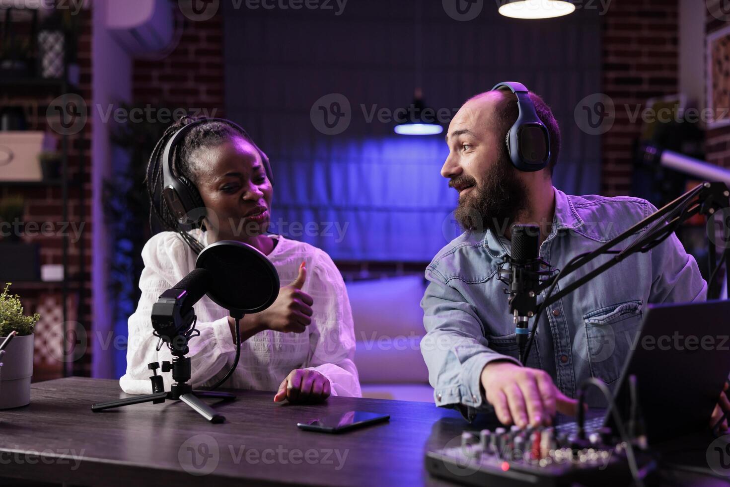 Experienced radio host playing music in professional on air studio, impressing african american guest showing thumbs up hand gesturing. Dj using high quality setup to stream musical production photo