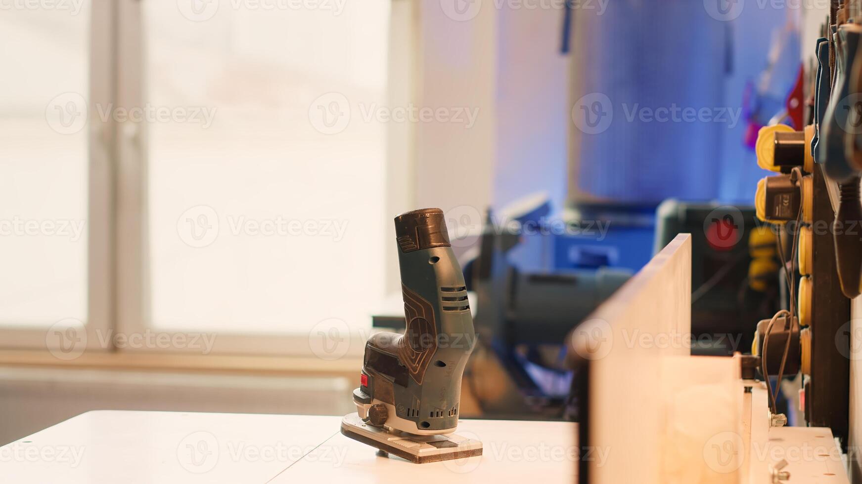 Close up of electric router on spindle moulder in furniture assembly shop with woodworking tools on rack in background. Focus on hand powered equipment used for sanding wood in studio, panning shot photo