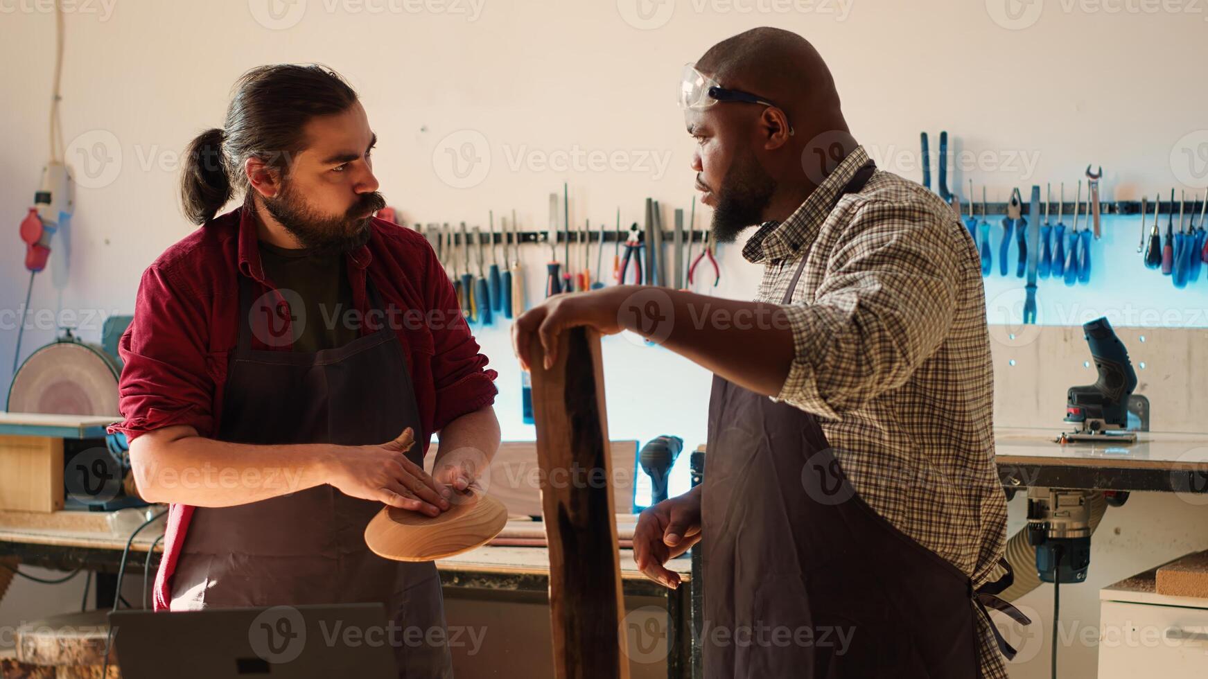 Woodworker looking over blueprints on laptop, brainstorming with colleague next steps in wood processing. Manufacturer and BIPOC apprentice reading furniture assembly schematics in studio, camera A photo