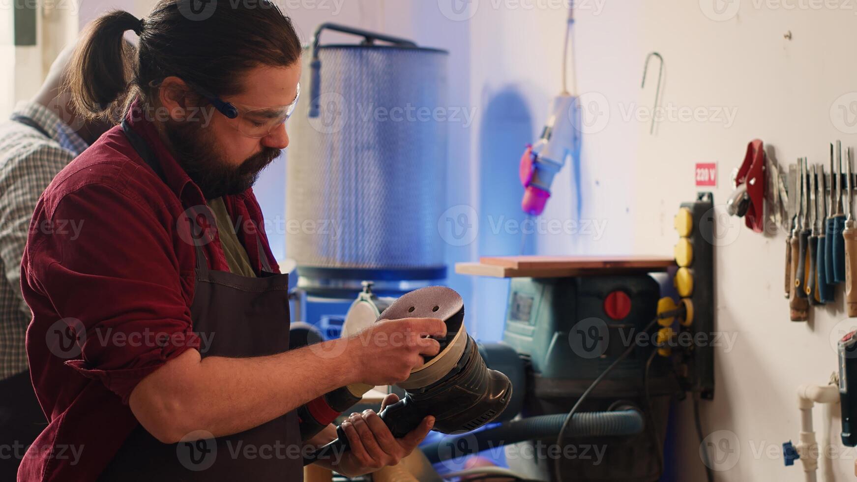 Carpenter holding power tool used to smooth surfaces by abrasion with sandpaper, changing cut off discs. Man preparing necessary equipment for furniture assembling job in studio, camera A photo