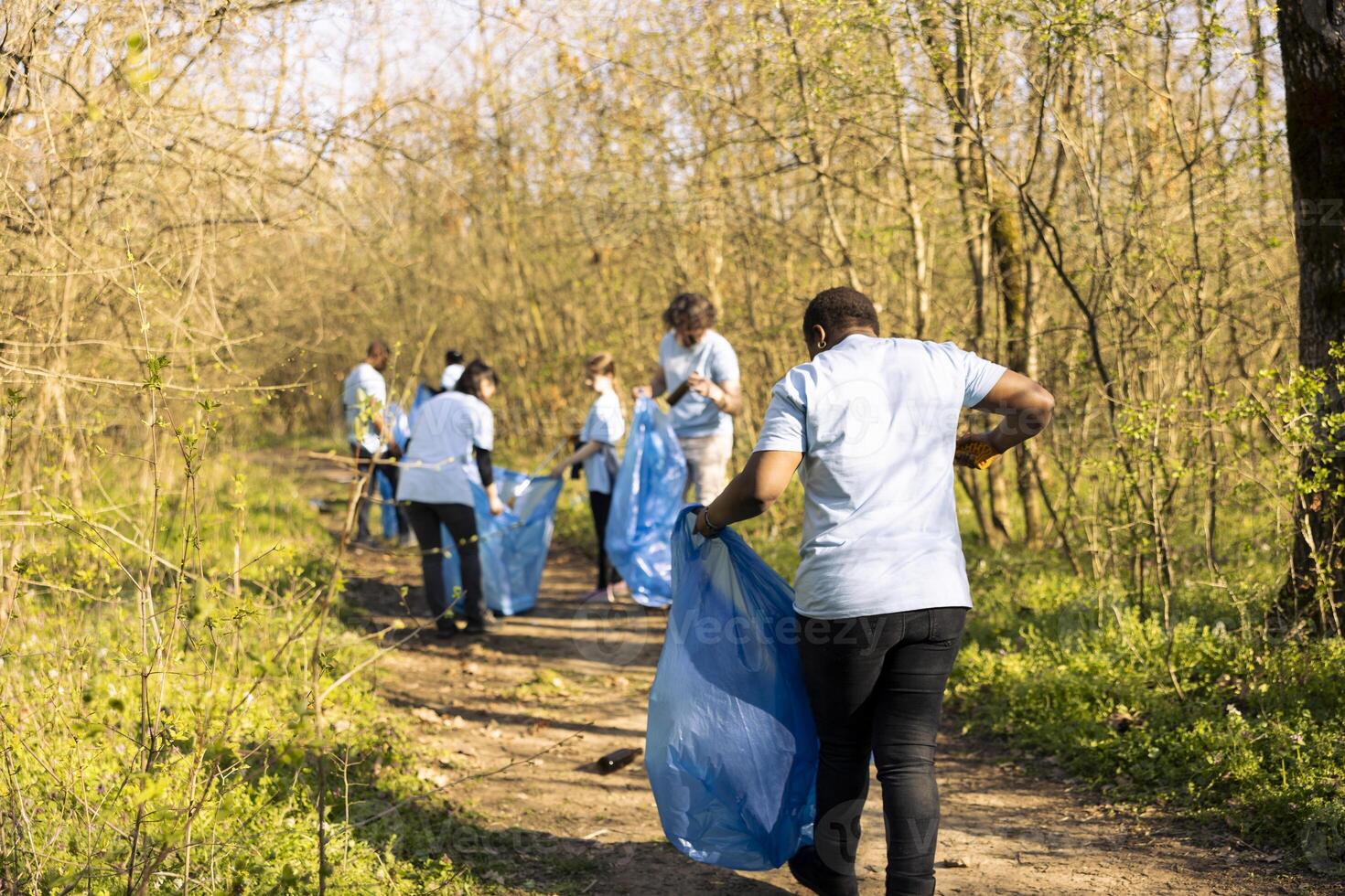 African american woman grabbing junk and plastic waste from the forest, doing voluntary work to preserve and protect the environment. Female activist using claw tool to collect garbage and junk. photo