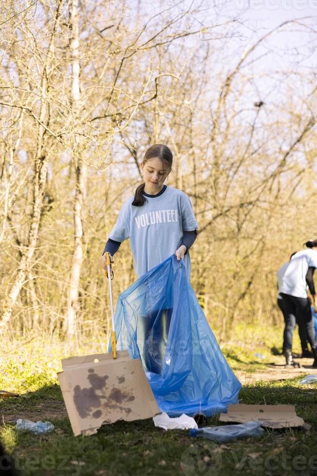Environmental activist child gathering trash and plastic litter in a bag, recycling rubbish in a disposal and cleaning the woods. Young girl supporting ecology and zero waste activism. photo