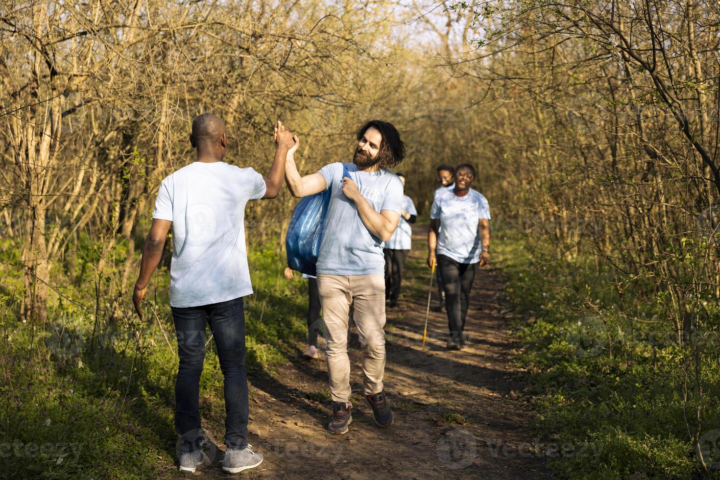 African american man sharing high five with his team of activists, praising each other after finishing forest garbage cleanup. Group of volunteers feeling proud and satisfied with their work. photo