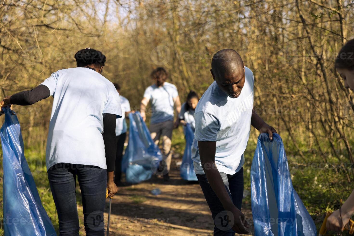 African american volunteers team working to clean the forest from trash, combat forest pollution to protect the natural habitat. Young man and woman activists collecting garbage. photo