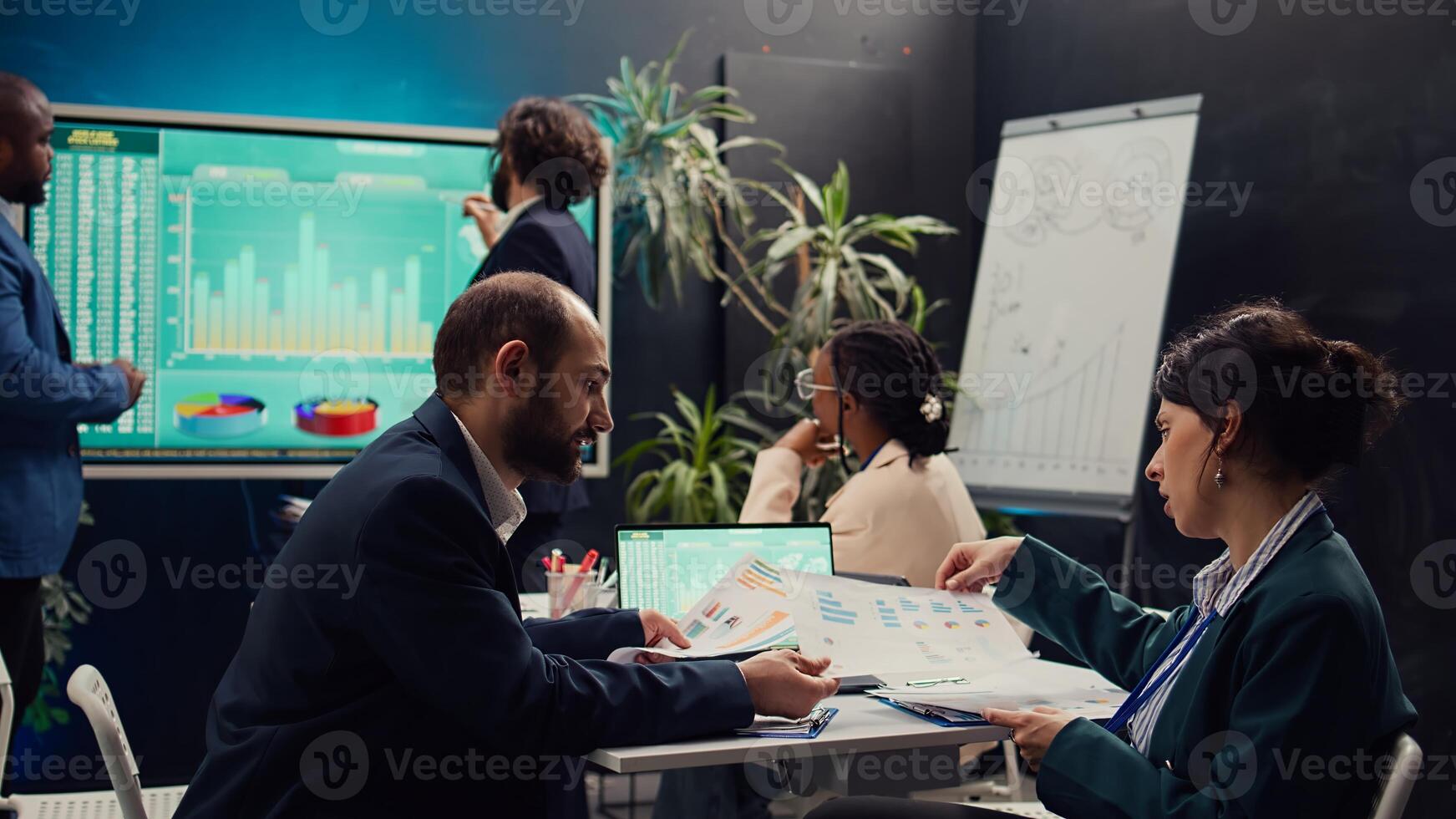 Public relations team creating marketing campaigns and promotional activities in a boardroom, collaborating on new development plan. Employees reviewing sales trends metrics on pc. Camera B. photo