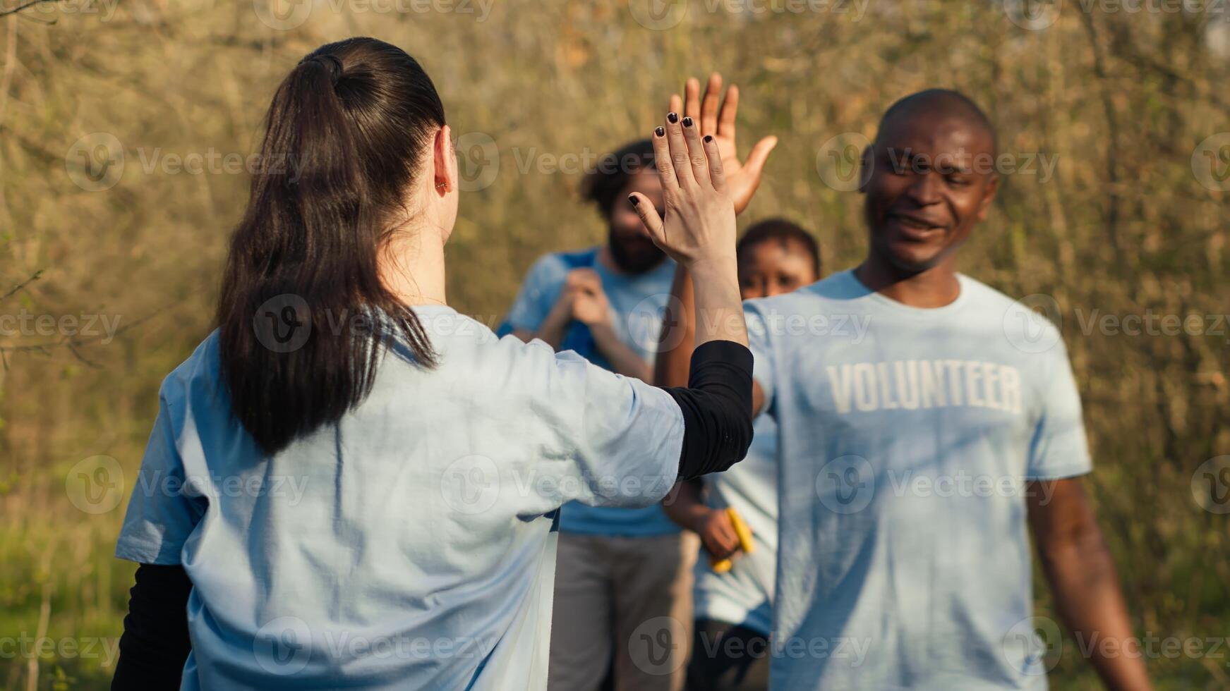 Activists congratulating each other with a high five after a successful teamwork, showing perseverance in collecting rubbish and plastic waste from forest environment. A job well done. Camera A. photo