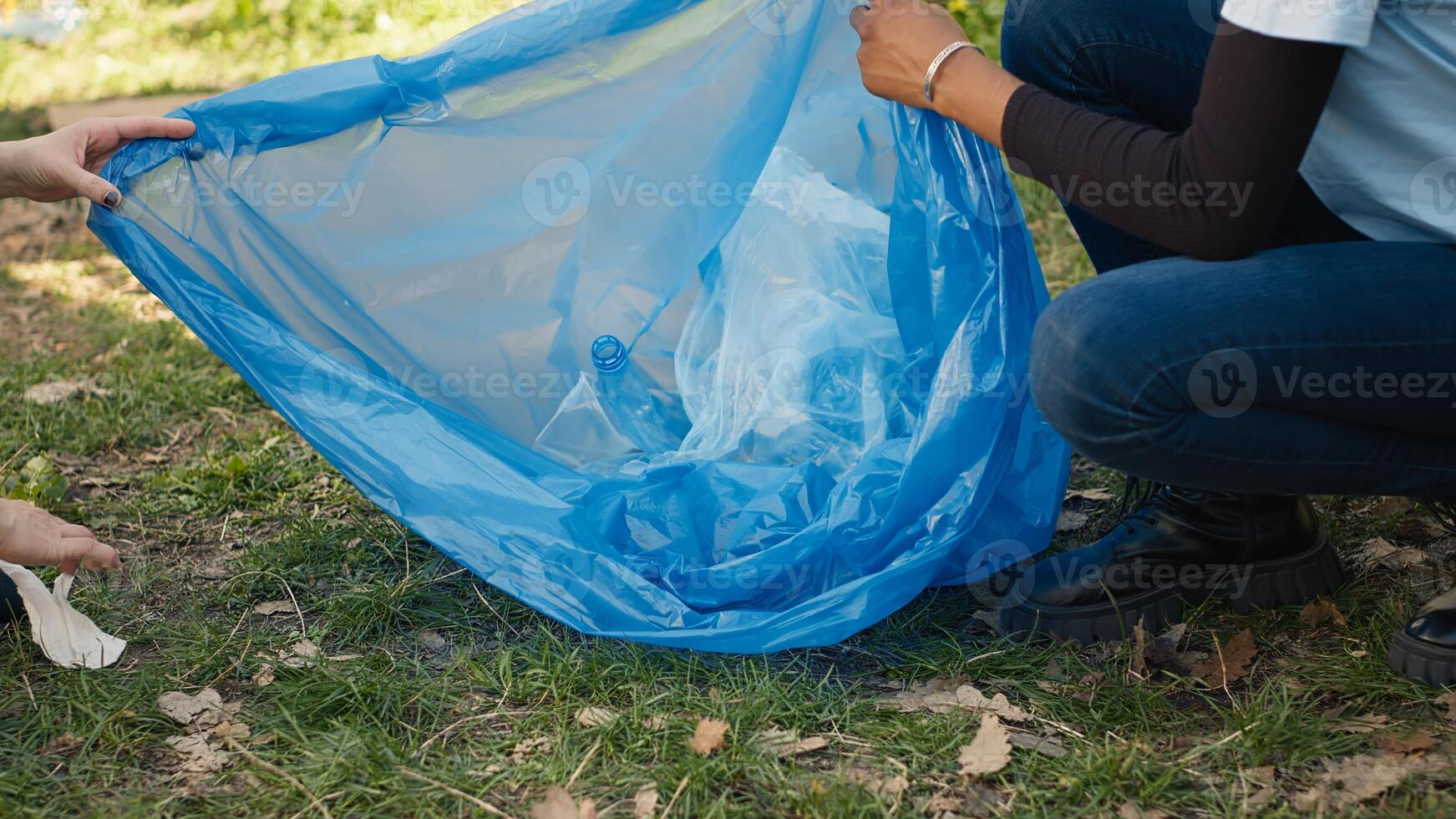 Team of activists collecting rubbish and plastic waste to recycle, cleaning the woods with litter cleanup tools and garbage bags. People picking trash from the forest, activism. Close up. Camera A. photo