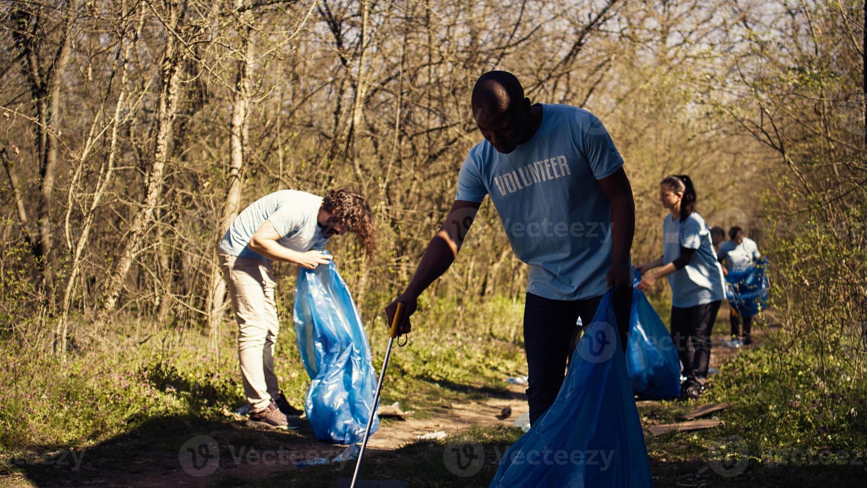 African american man volunteer collecting trash and plastic waste with tongs, grabbing rubbish and recycling in a garbage disposal. Activist combating forest pollution and illegal dumping. Camera B. photo