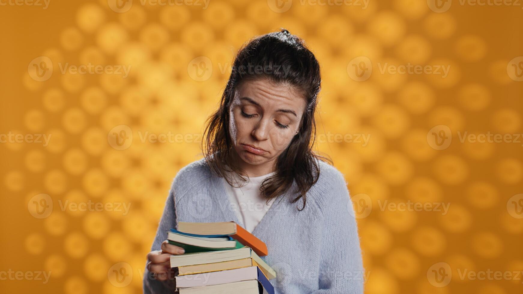 Portrait of woman browsing through stack of textbooks, gathering information for school exam, isolated over studio background. Person searching necessary course for exam in pile of books, camera B photo