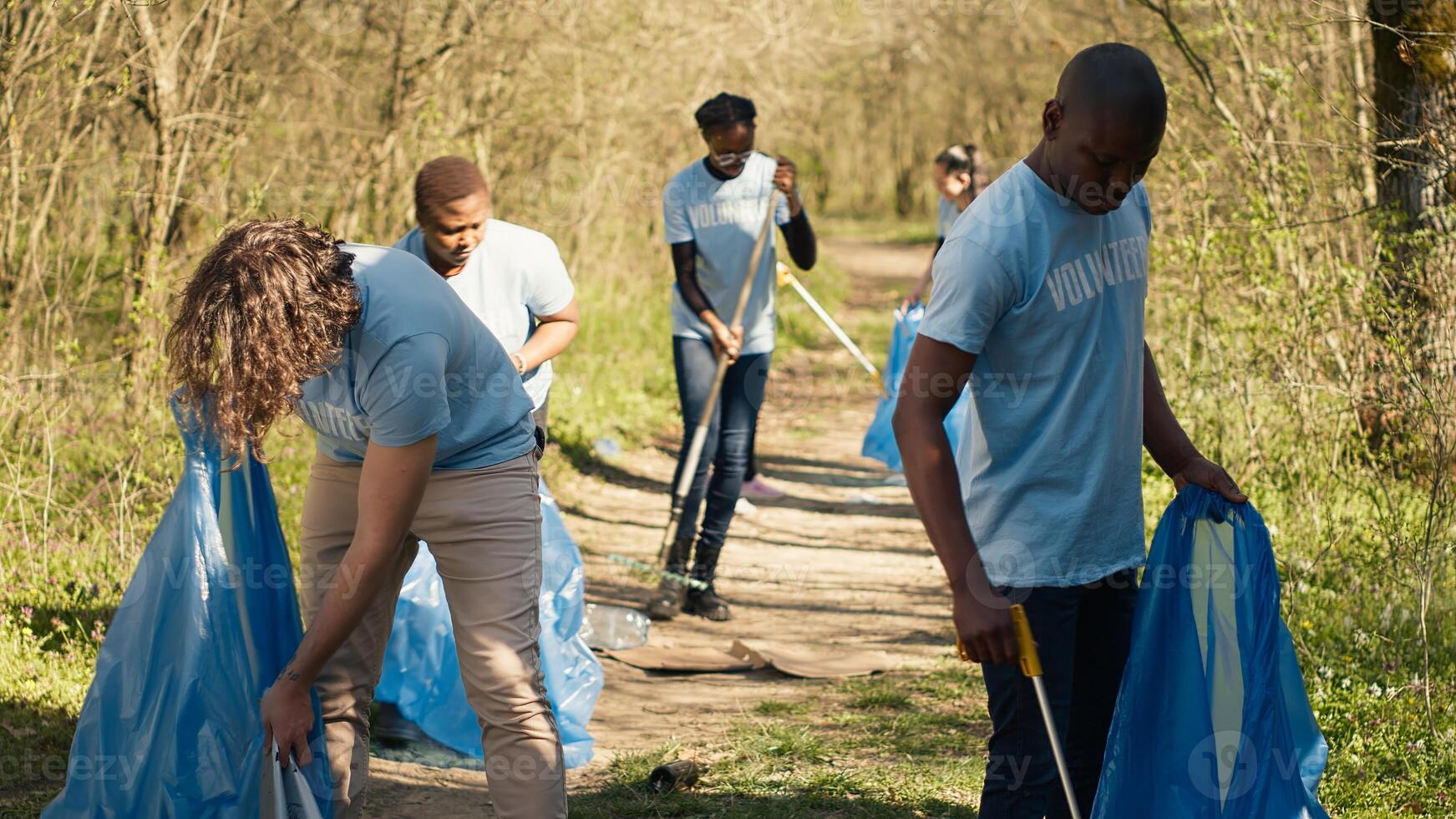 Diverse men volunteers pick up rubbish and plastic trash with tongs, working to combat illegal dumping and preserve natural forest environment. Activists volunteering for litter cleanup. Camera A. photo