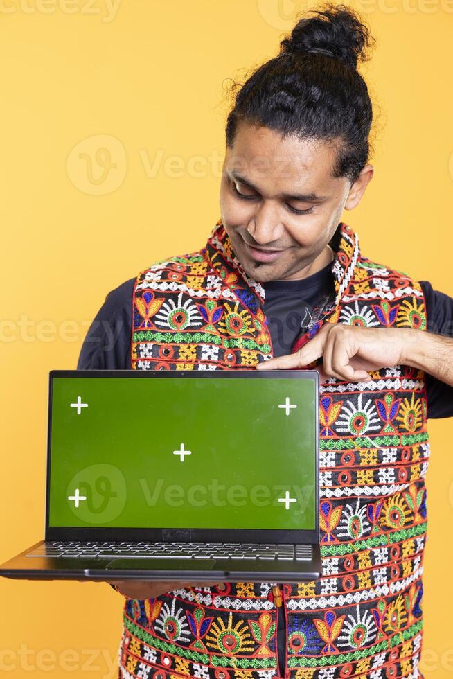 Radiant tech specialist presenting green screen laptop, isolated over studio backdrop. Merry content creator reviewer giving positive feedback while showcasing chroma key notebook photo