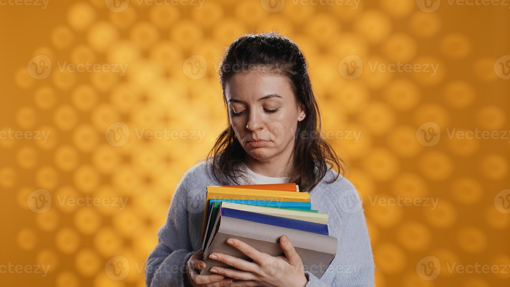 Exhausted woman yawning, holding heavy stack of books needed for school exam, studio background. Student yearning for sleep, tired of learning from academic textbooks, camera B photo