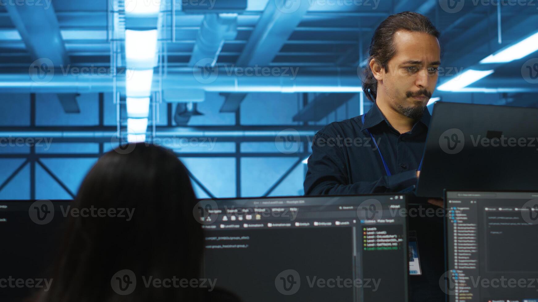Portrait of smiling manager using laptop, supervising team in server hub providing computing resources for workloads. Happy team leader oversees engineers in data center mending supercomputers photo