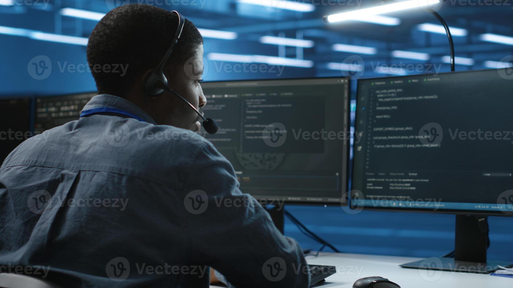 IT support worker in data center talking in headset mic with coworkers, coding on computer. Man discussing with colleagues using headphones microphone, overseeing server clusters photo