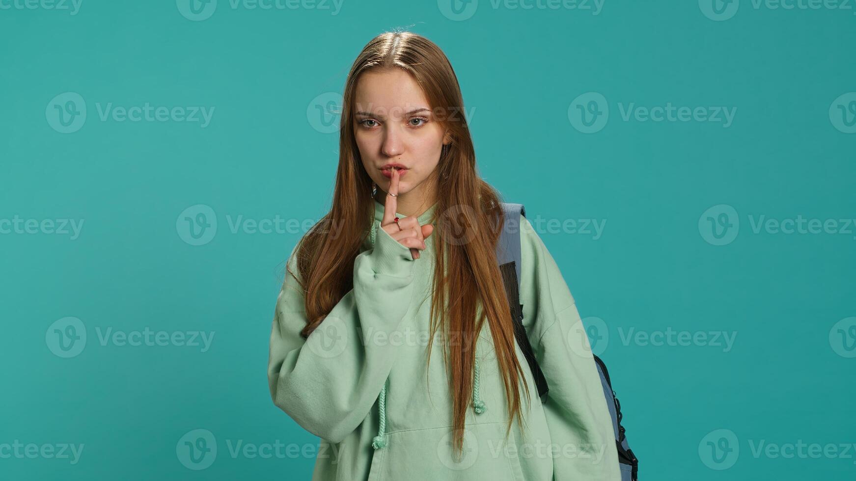 Stern woman doing shushing hand gesturing, irritated by noise, having negative mood. Girl placing finger on lips, doing quiet sign gesture, isolated over studio background, camera A photo