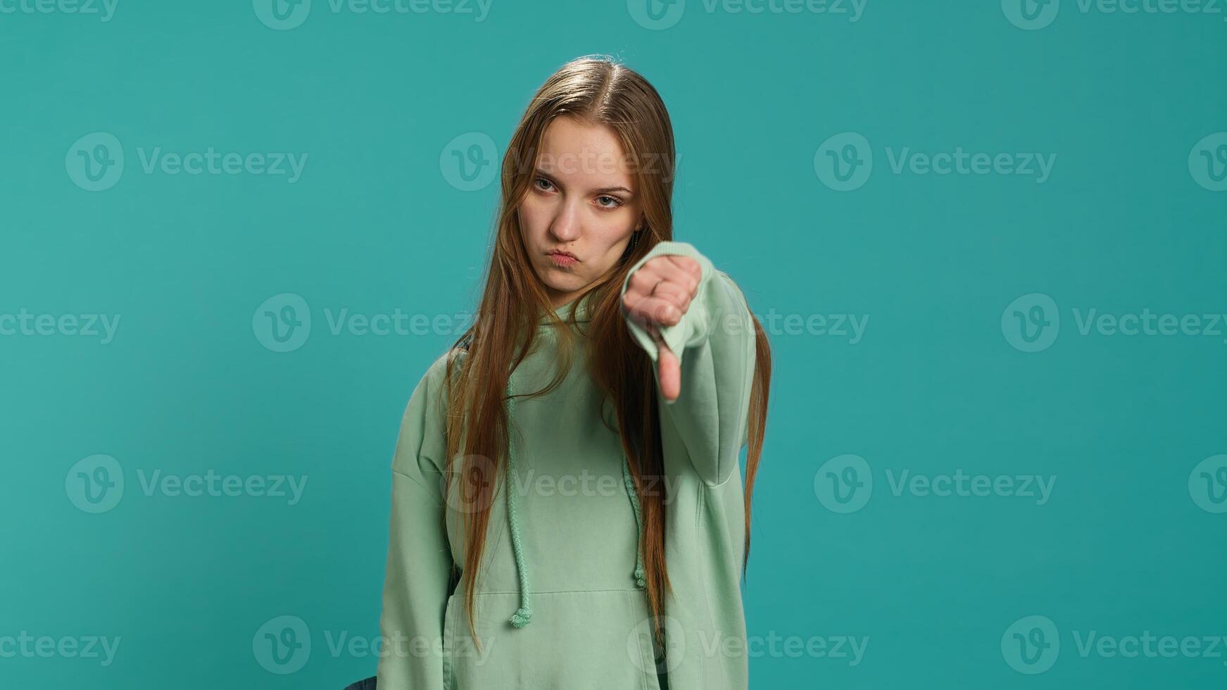 Frustrated woman showing thumbs down sign gesturing, disapproving and offering negative feedback. Disappointed girl doing dislike hand gesture, studio background, camera A photo