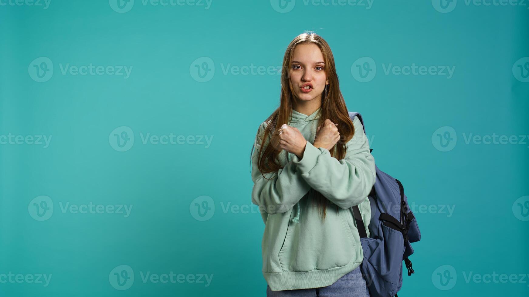 Assertive woman shows letter X with arms crossed, staying in warrior stance, showing fierceness. Firm young person using negative body language to signal rejection, studio background, camera B photo