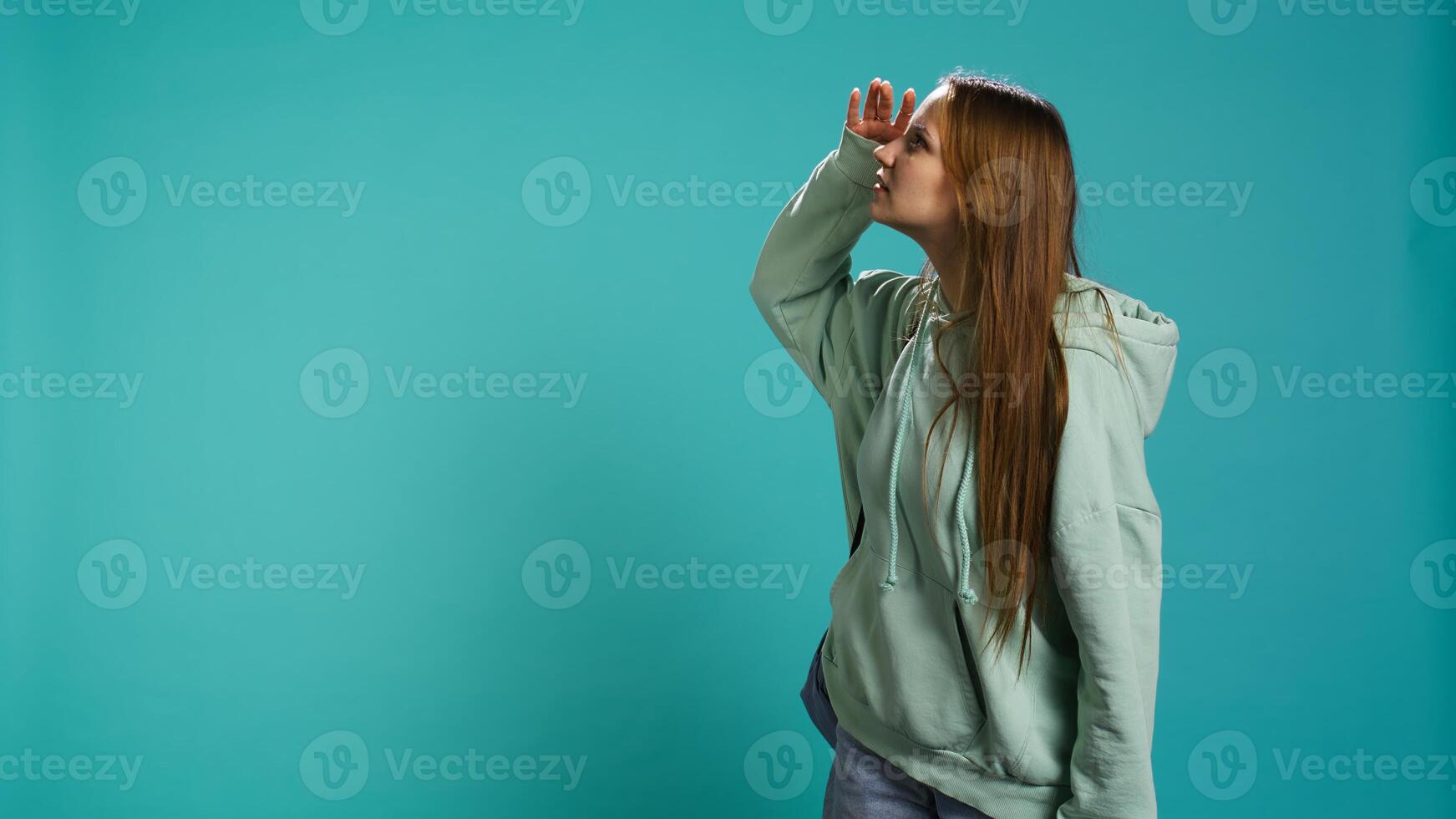 Portrait of jolly young woman holding backpack looking around for something, doing hand gesture. Joyous person analyzing horizon, seeking things, studio backdrop, camera B photo