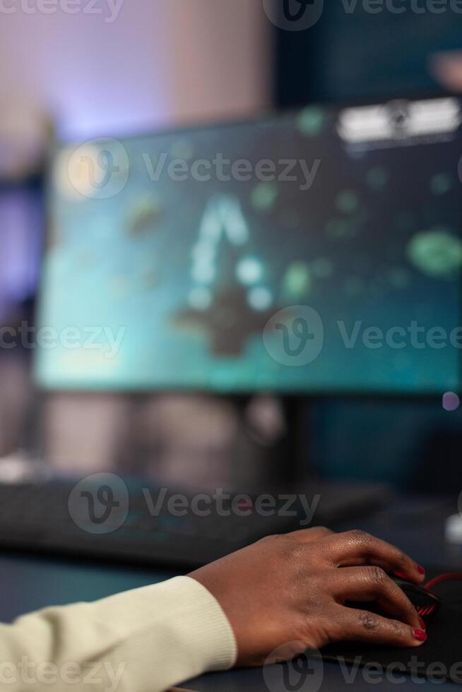 Close up of african american gamer holding hand on computer mouse playing space shooter games during online championship. Pro player woman using RGB gaming equipment in home studio photo