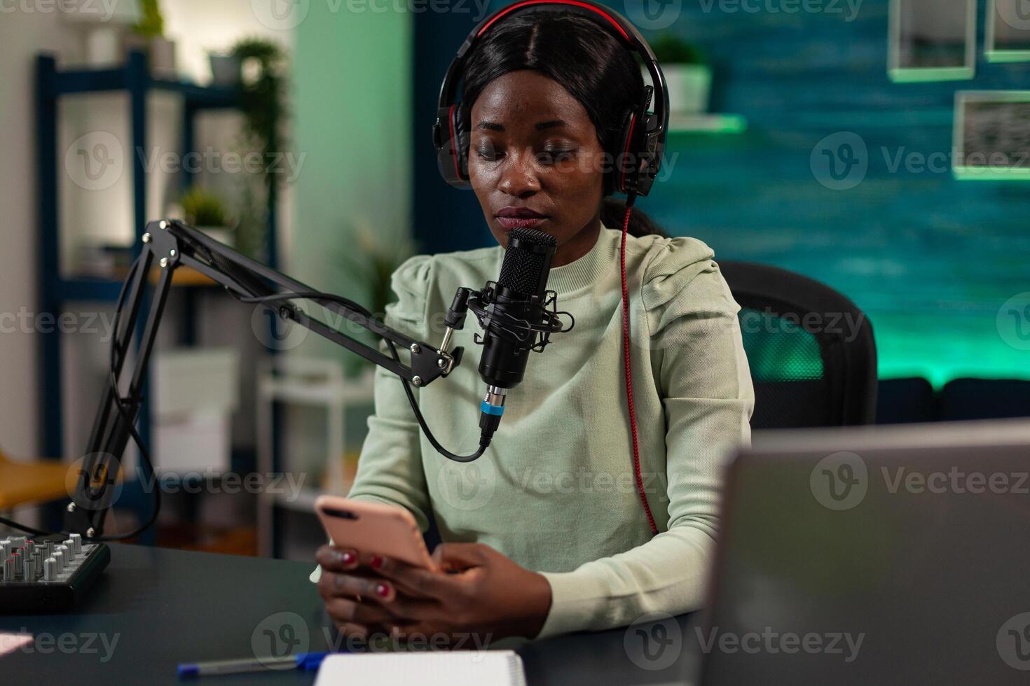 Social media content creator holding smartphone reading subscribers questions answering during live stream using vlogging microphone. Woman vlogger recording online in filming home studio photo