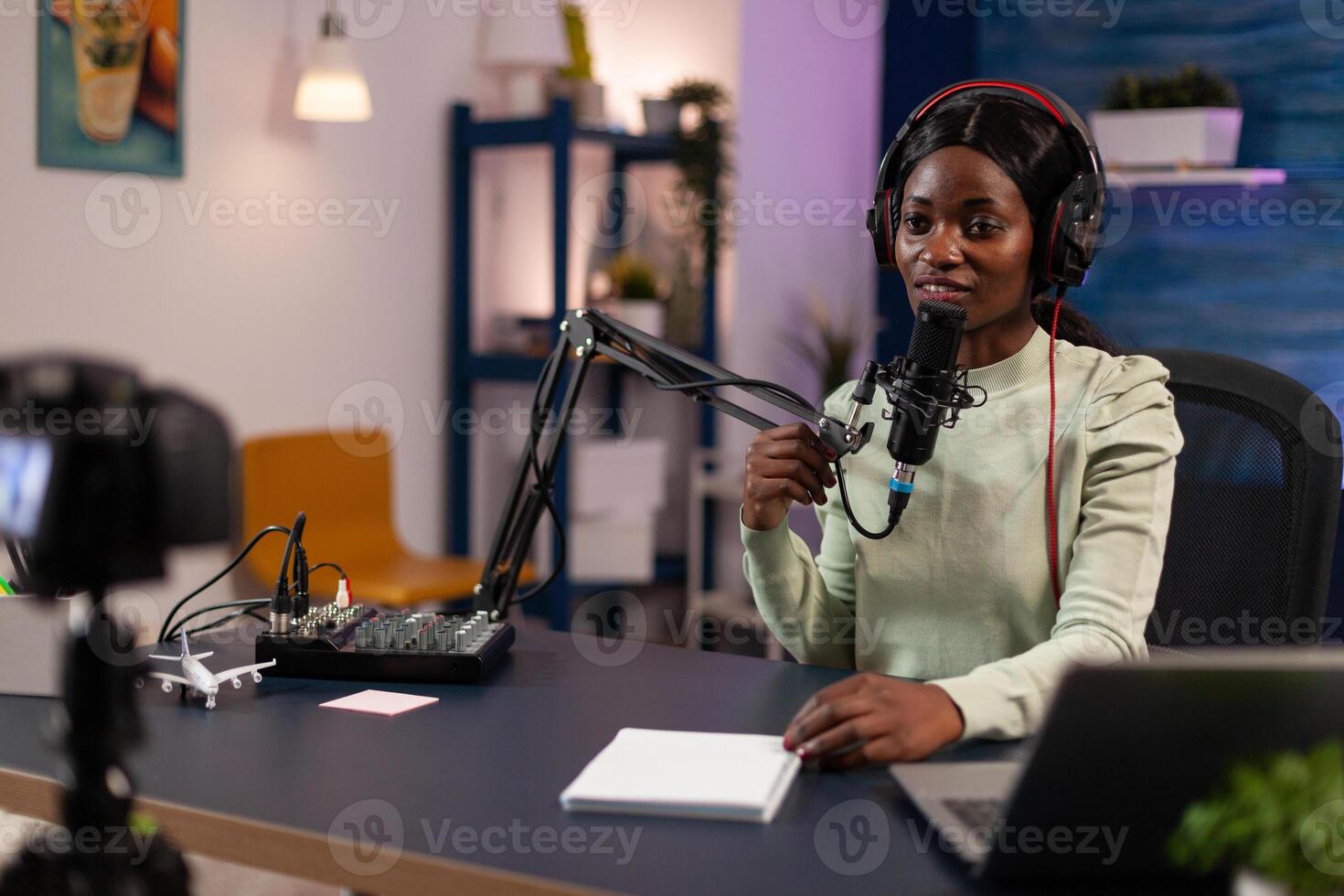 Social media influencer woman talking into production microphone answering subscribers questions while recording content sitting in filming studio at home. Vlogger hosting on air live show photo