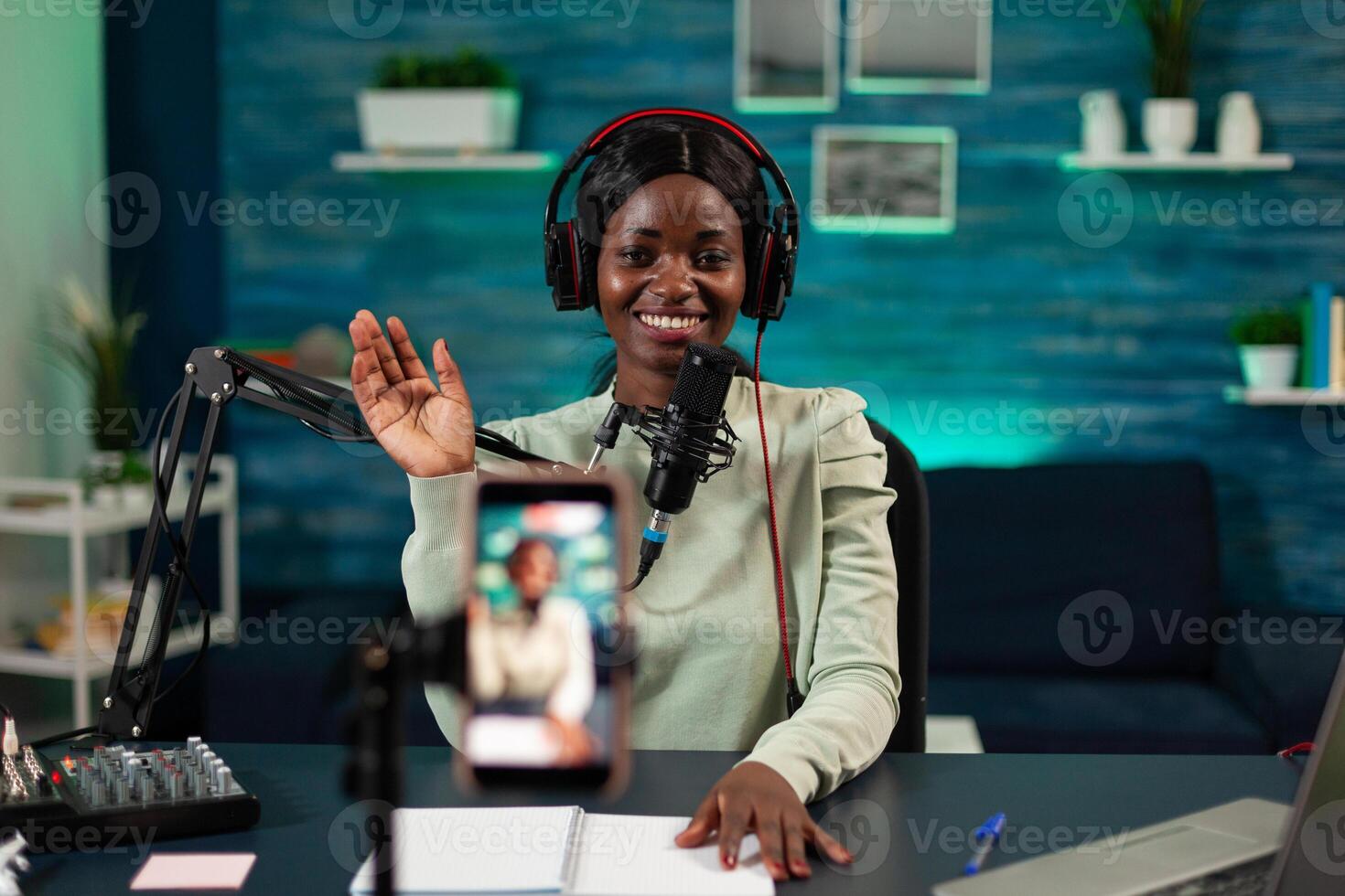 Podcast creator sitting at desk in vlogging studio greeting subscribers while recording content for youtube channel. Social media influencer filming vlog talking into production micophone photo