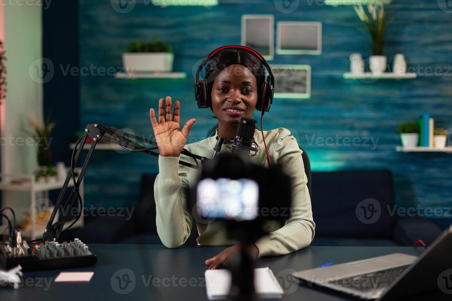 African american vlogger woman greeting subscribers while recording content for social media. Influencer sitting in podcast studio filming tutorial using production equipment. On air talk show photo